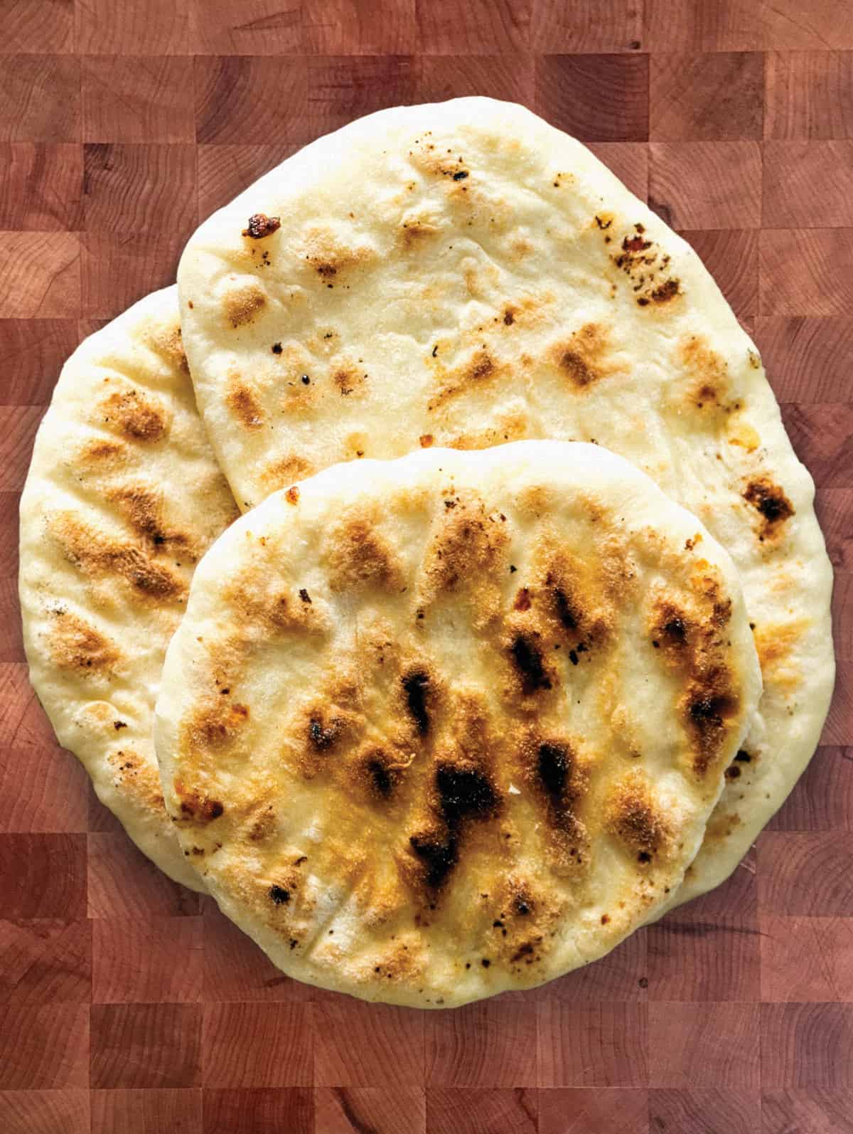 A flatbread, a naan bread and a pita on a table.