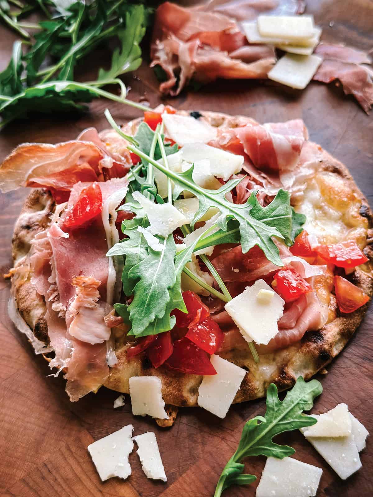 A pita pizza with prosciutto and arugula on a wooden table.