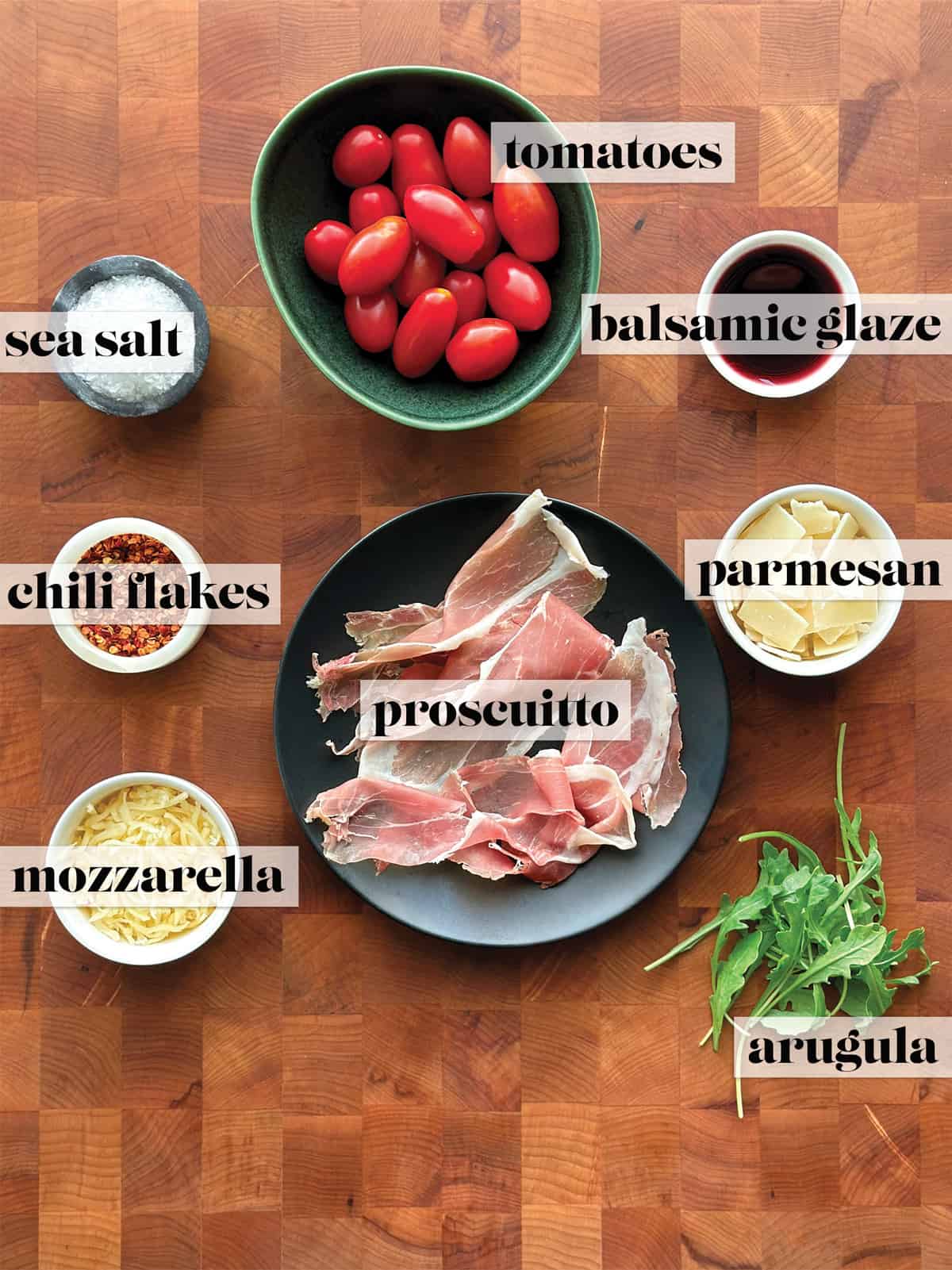 Bowls with cherry tomatoes, prosciutto, mozzarella cheese , olive oil, balsamic glaze, parmesan cheese flakes, fresh arugula, chili flakes and sea salt, all the Ingredients to make gyro pita pizza.