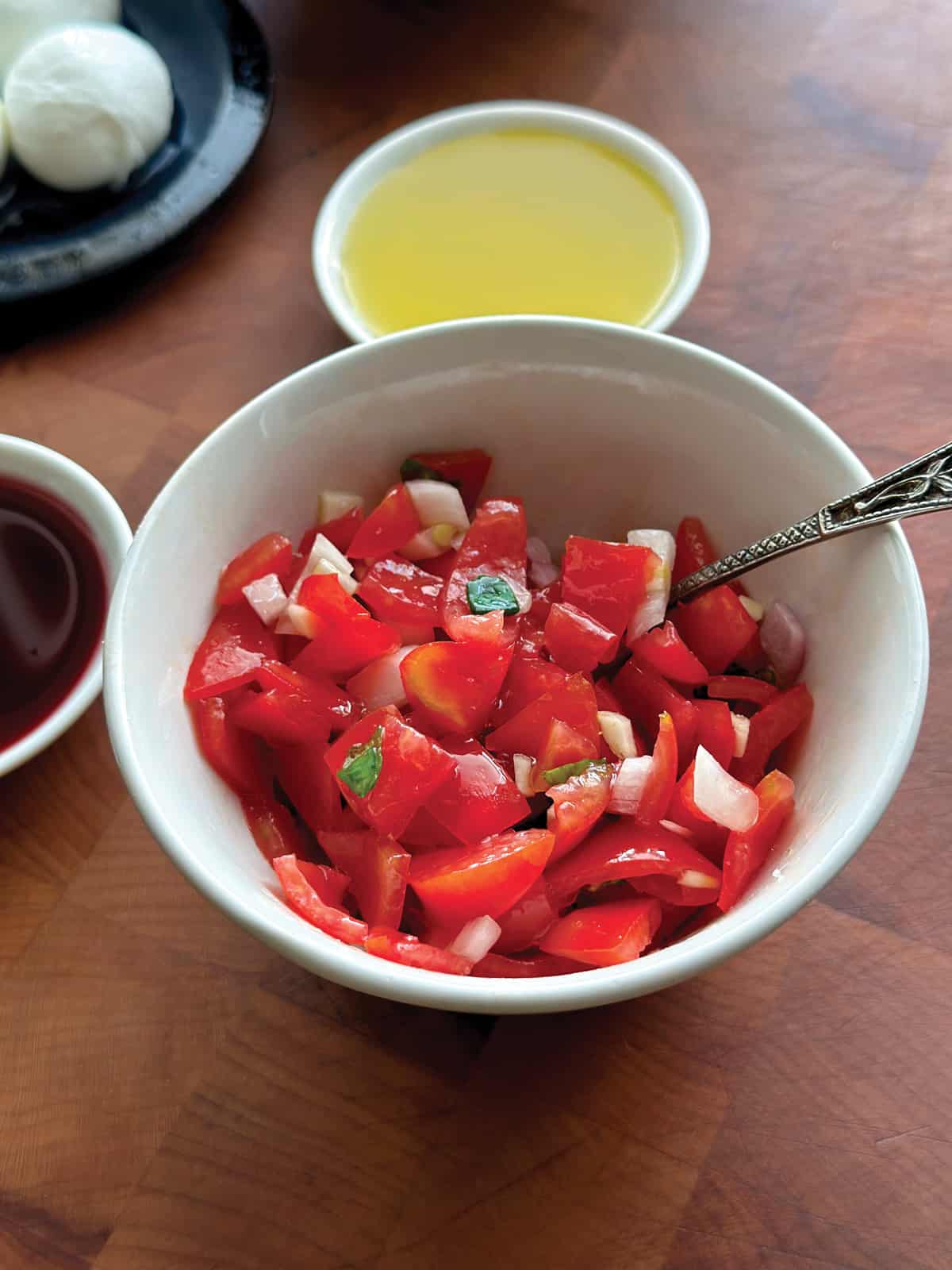 A bowl with diced tomato salad next to a small plate with olive oil.