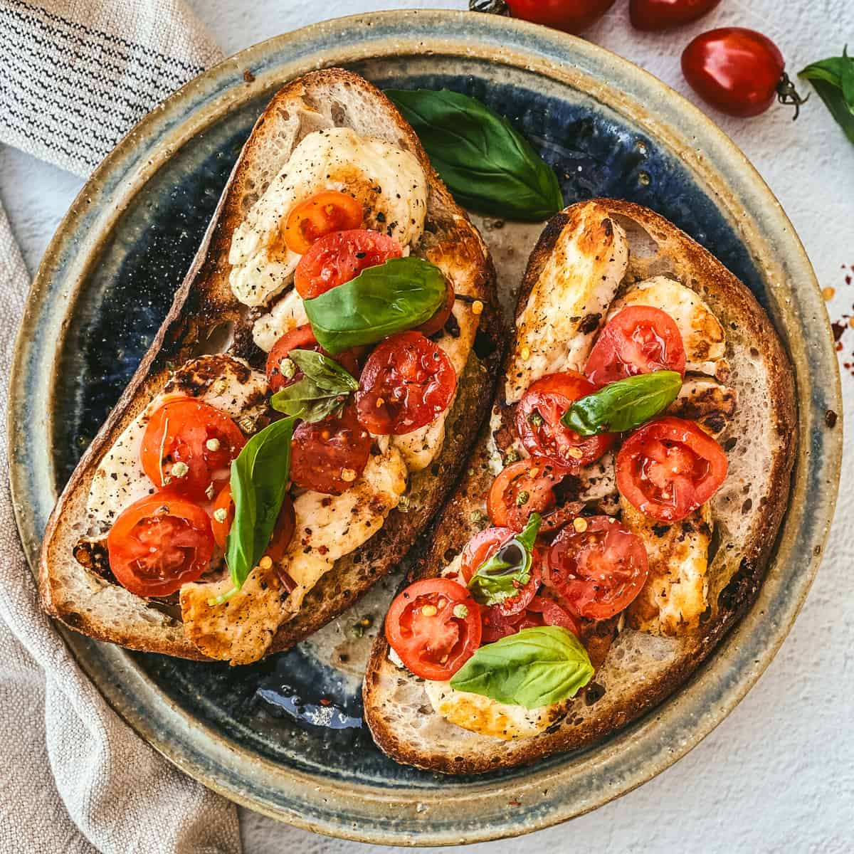 Fried halloumi and tomatoes on toast, on a plate with a cloth napkin, tomatoes and fresh herbs.