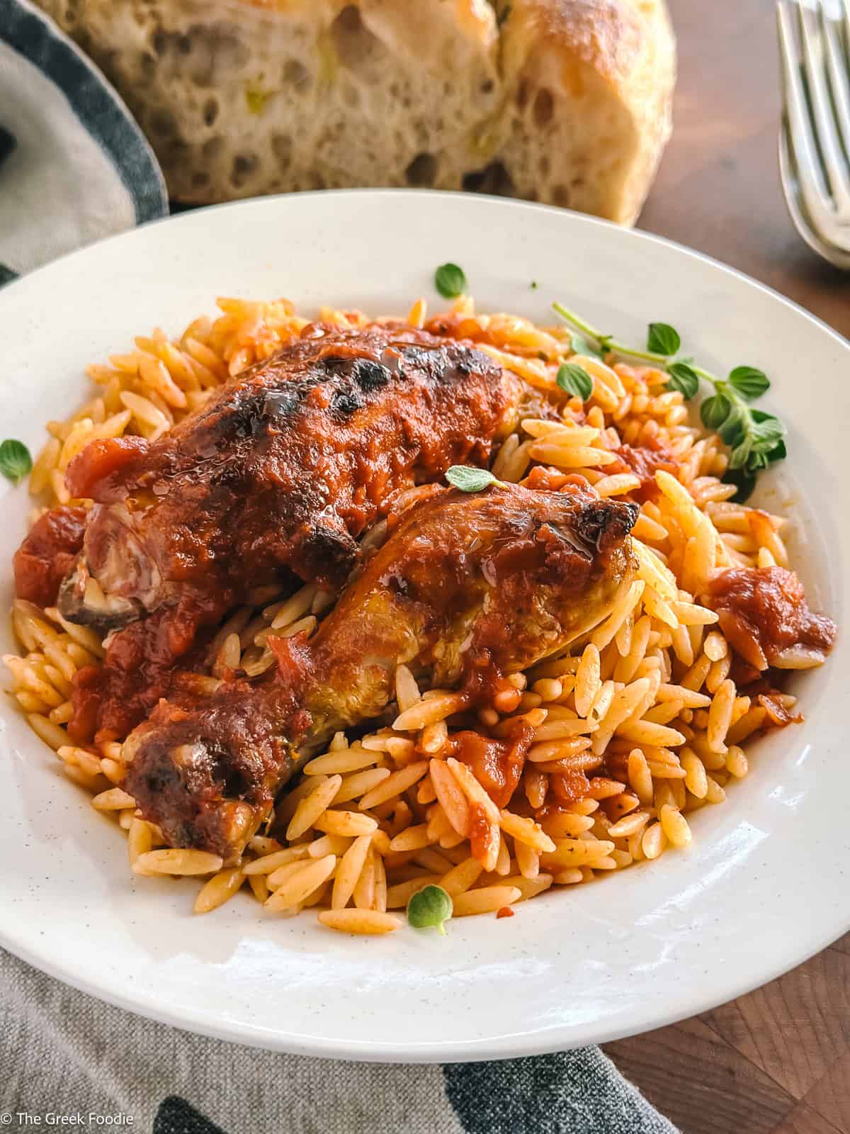 A serving of Greek chicken orzo youvetsi, a browned chicken piece resting on saucy orzo.