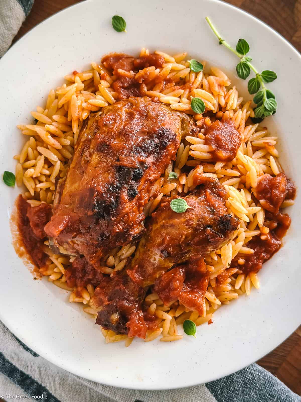 Overhead of Greek chicken youvetsi on a white plate, browned chicken thighs over orzo- kritharaki in tomato sauce.