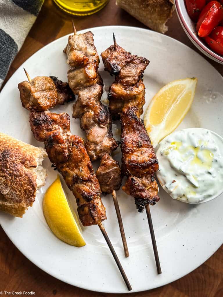 Greek pork souvlaki Kalamaki skewers with bread, tzatziki and lemon wedges