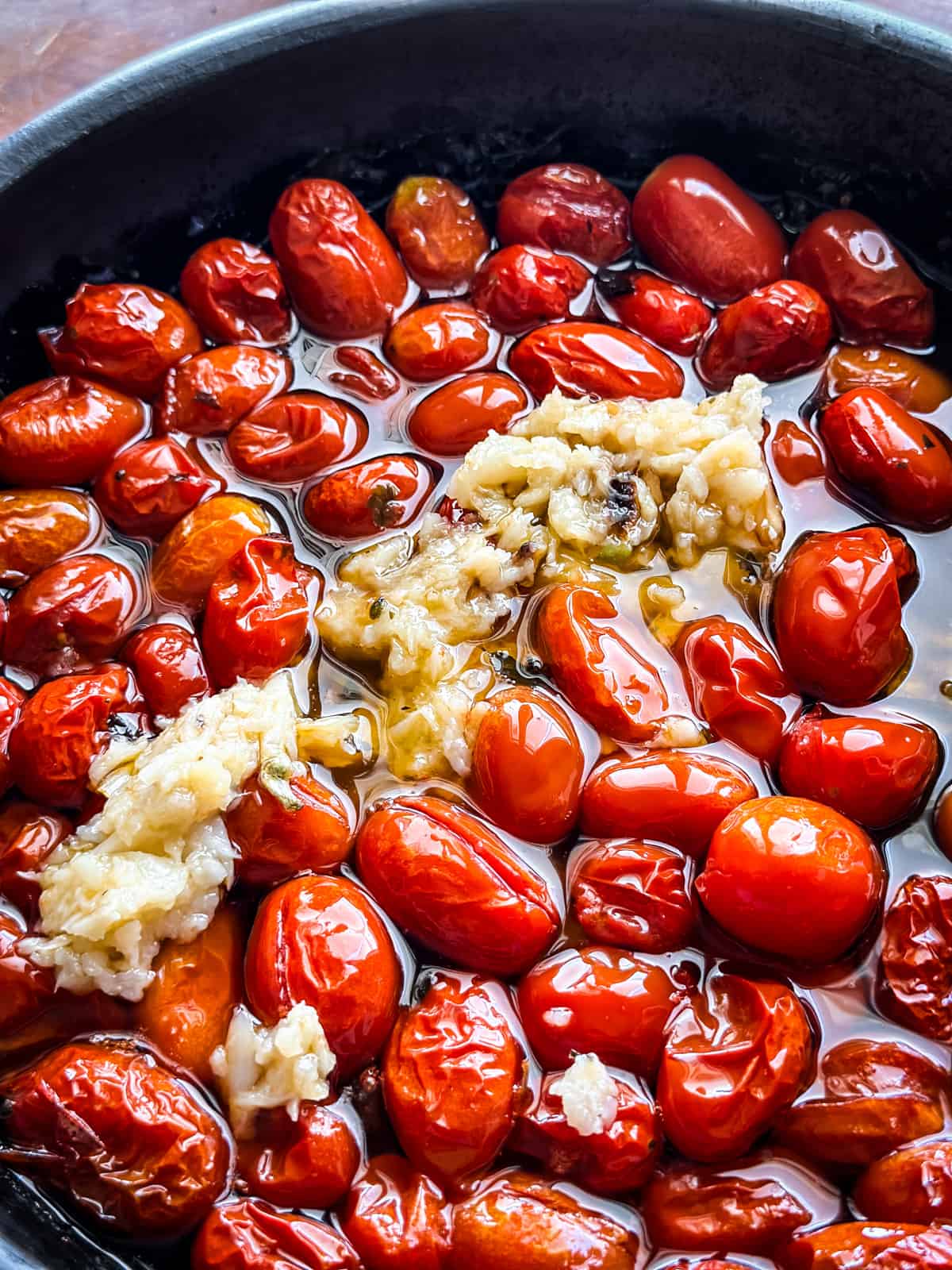 Close up of roasted tomatoes and mashed roasted garlic on top.