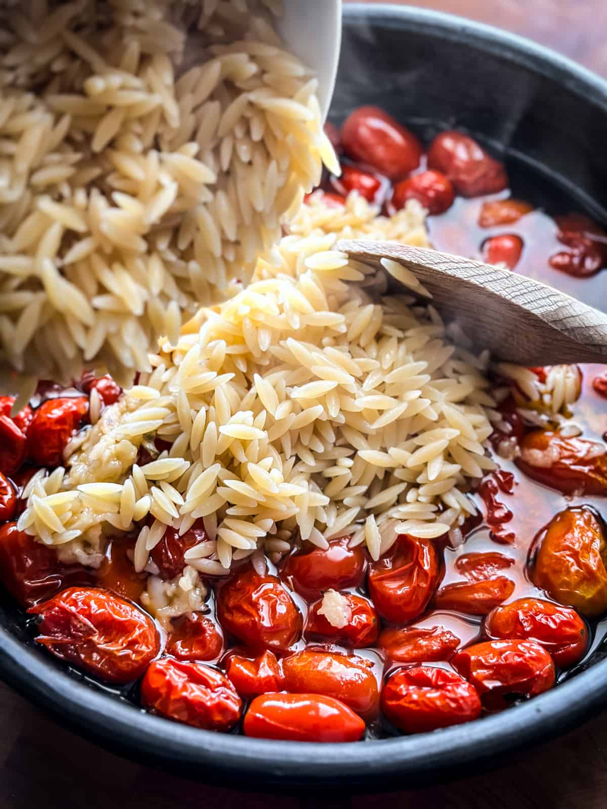 Close up of cooked orzo being added to roasted tomatoes.