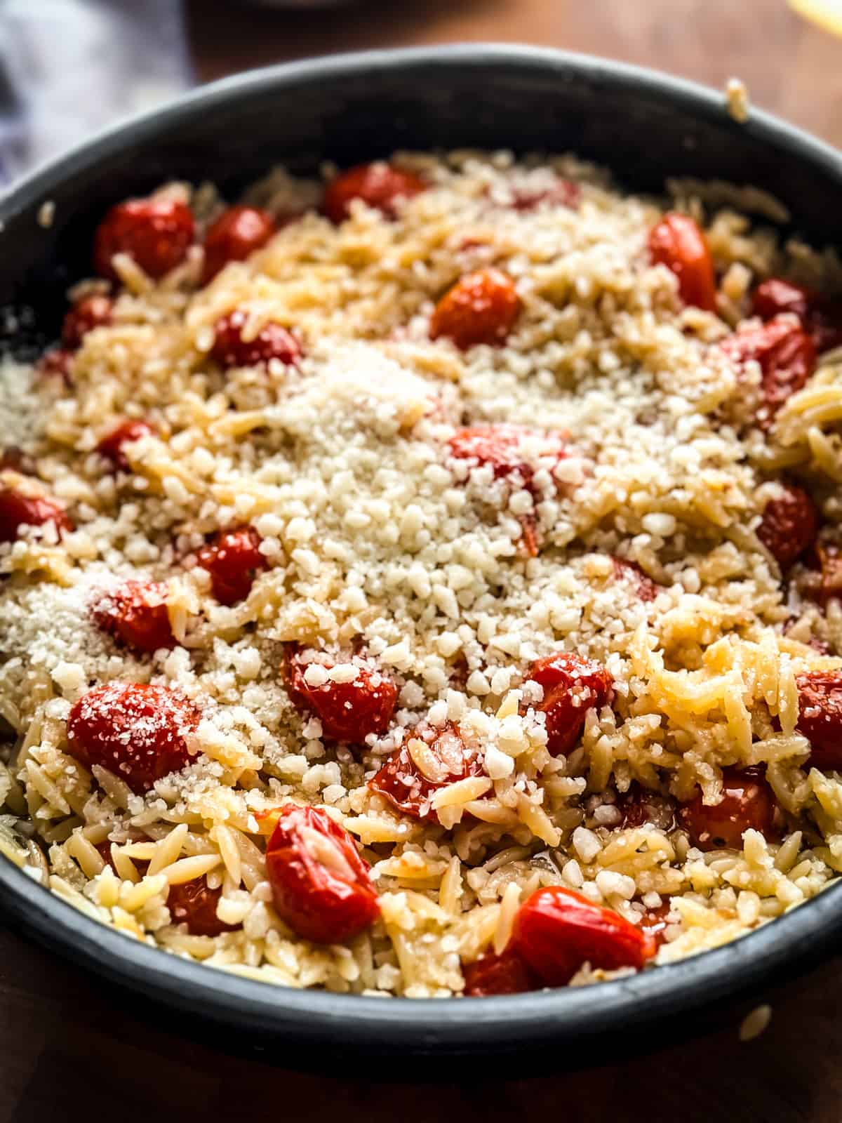 A round baking pan with orzo pasta, tomatoes, and grated parmesan on top.
