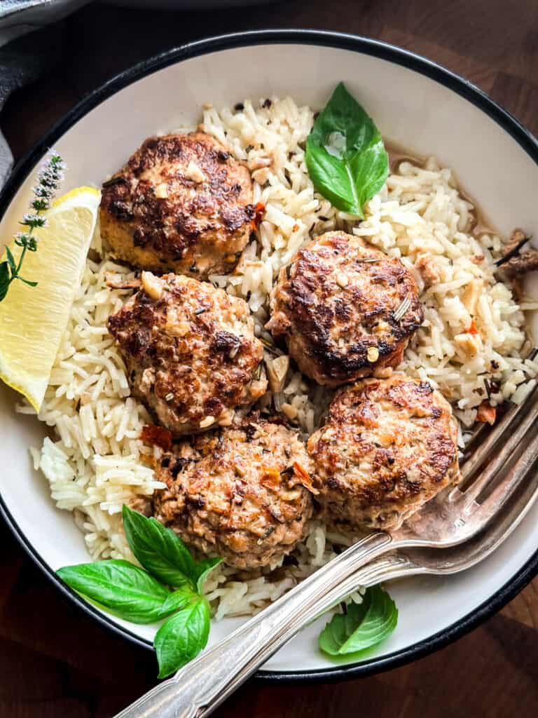 Chicken meatballs on lemon rice in a plate with a lemon wedge and utensils.