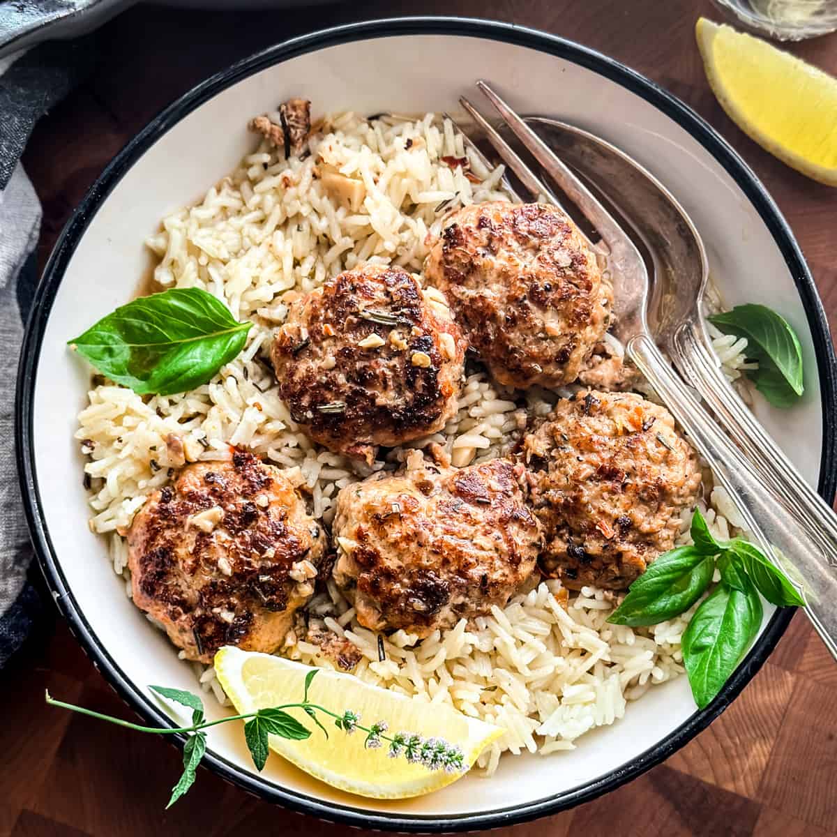 Chicken meatballs on lemon rice in a plate with a lemon wedge and utensils.