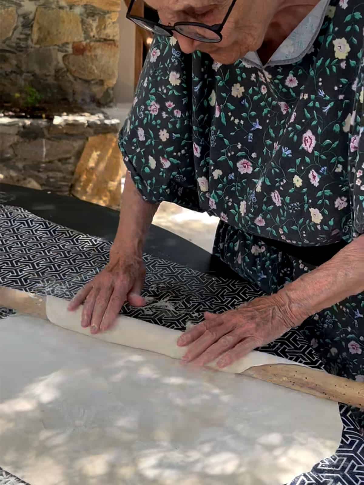 An elderly lady rolling the dough into a large phyllo sheet.