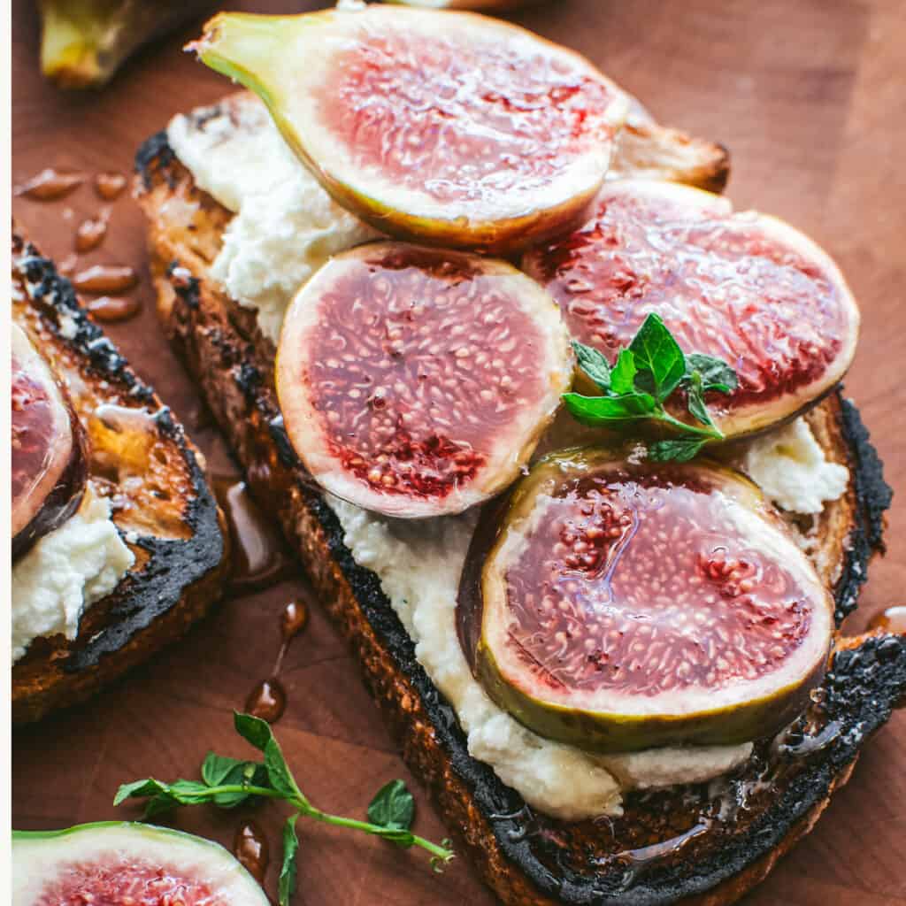 A fig toast with feta, herbs and honey on a table.