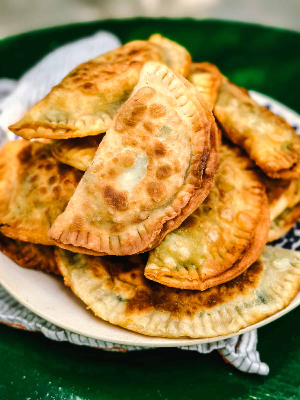 Kalitsounia, Cretan hand pies from Chania in a plate with a cloth napkin on a dark green table.