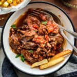 A plate on table with kokkinisto-Greek braised beef in tomato sauce, three potato fries and utensils.