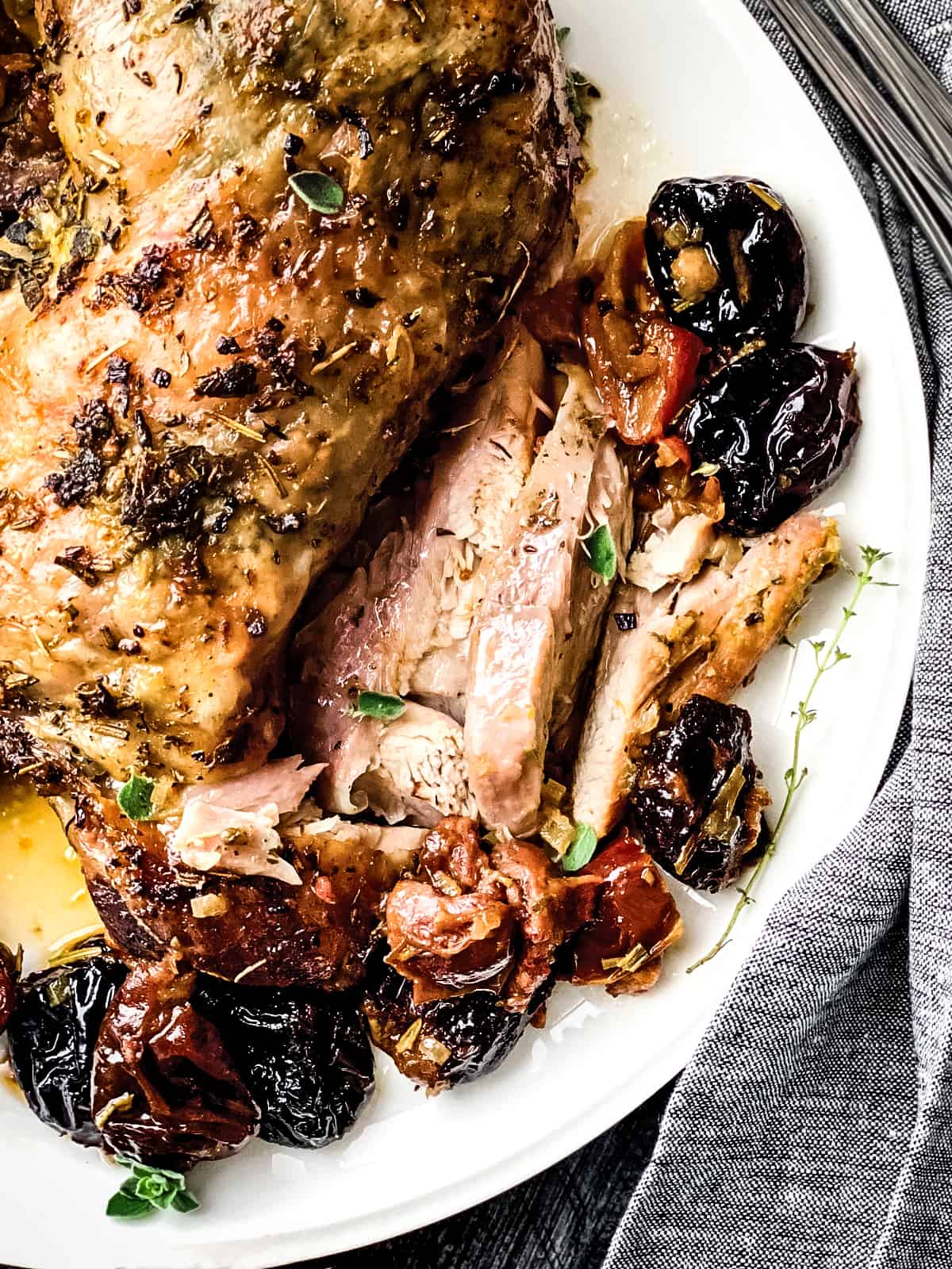 A roasted turkey thigh with sliced meat, some fresh herbs and dried fruit on a plate.