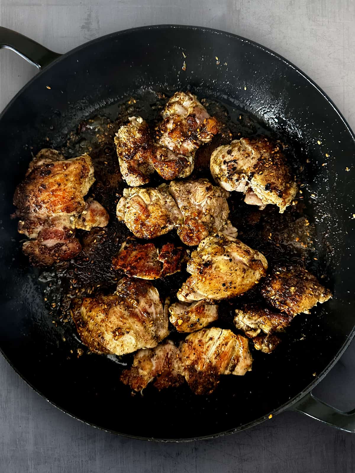 A large deep skillet cooking skinless chicken thighs.