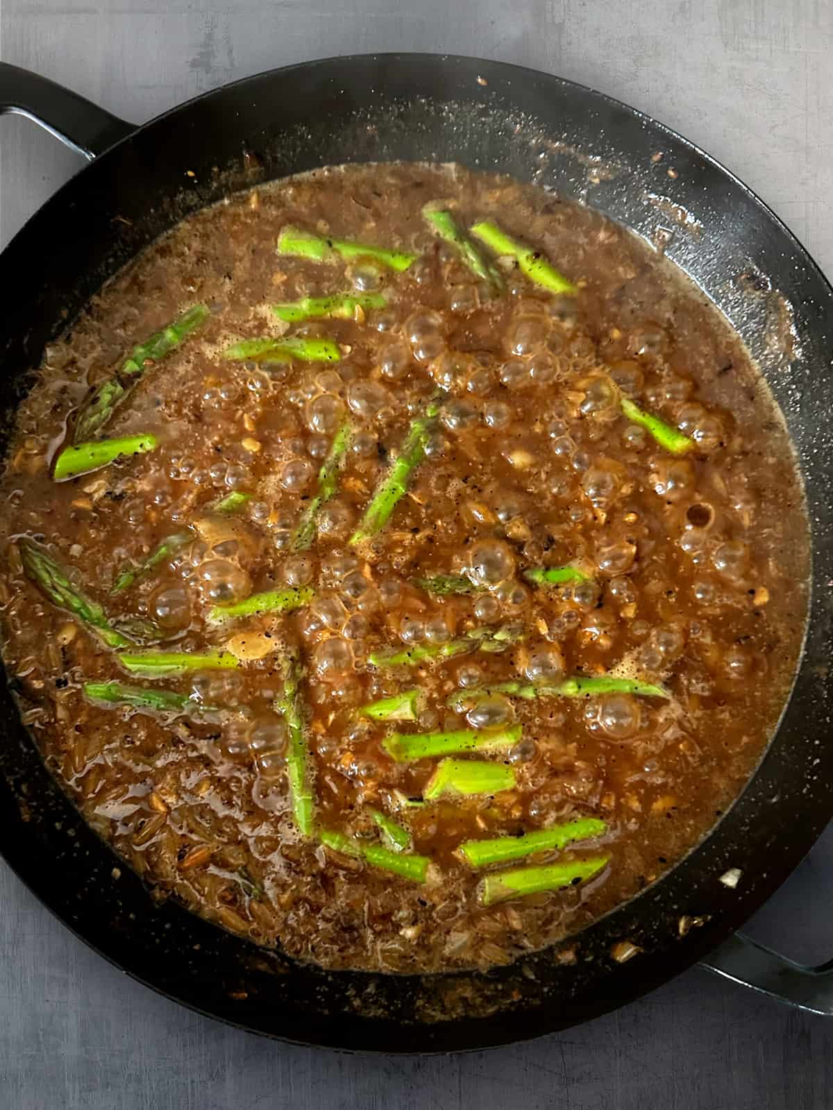 A large deep skillet with broth, orzo and asparagus tips.