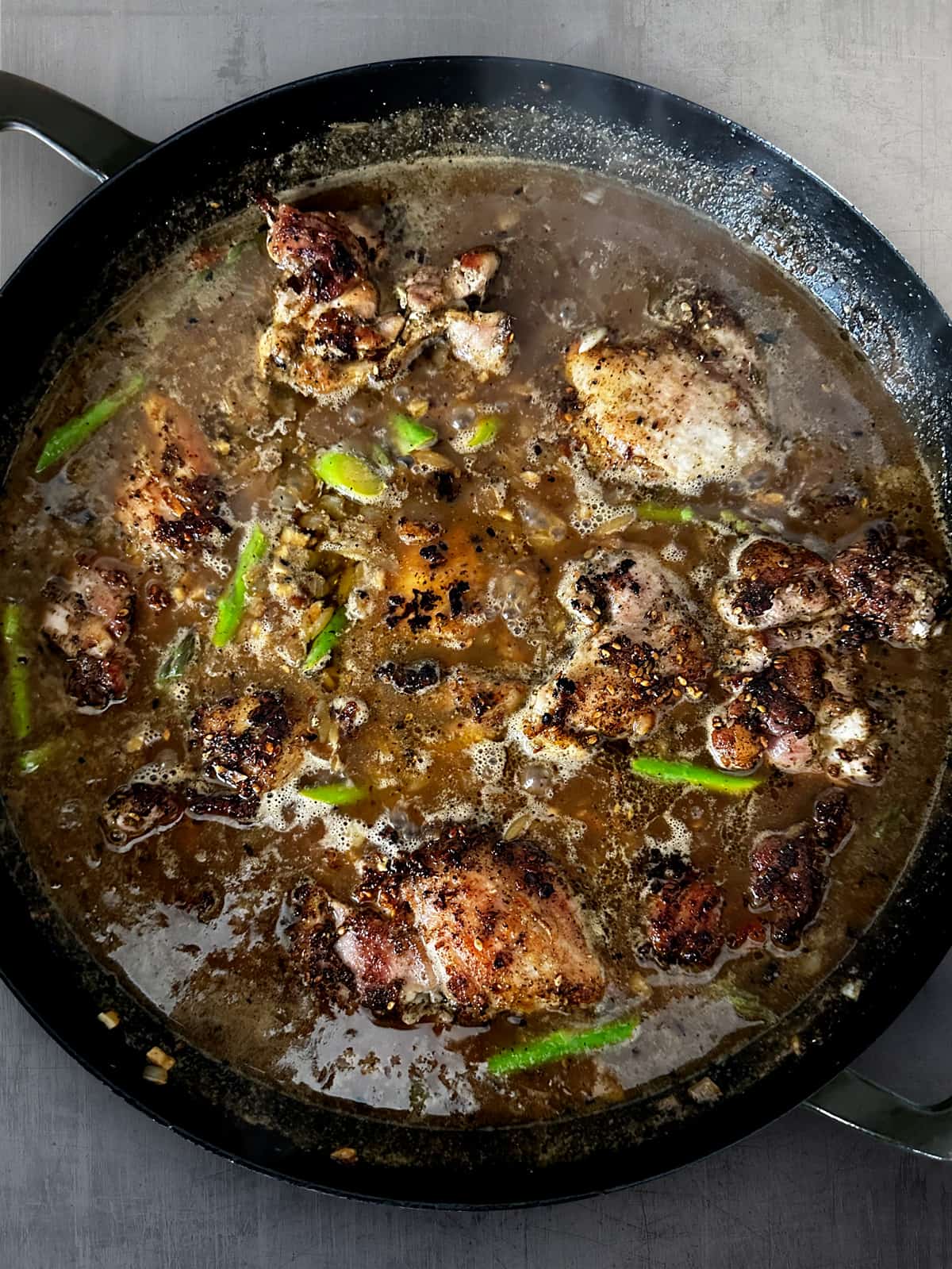 A large deep skillet with chicken thighs, broth, orzo and asparagus tips.