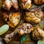 Greek chicken chops in a roasting pan with lemon wedges and fresh basil leaves.