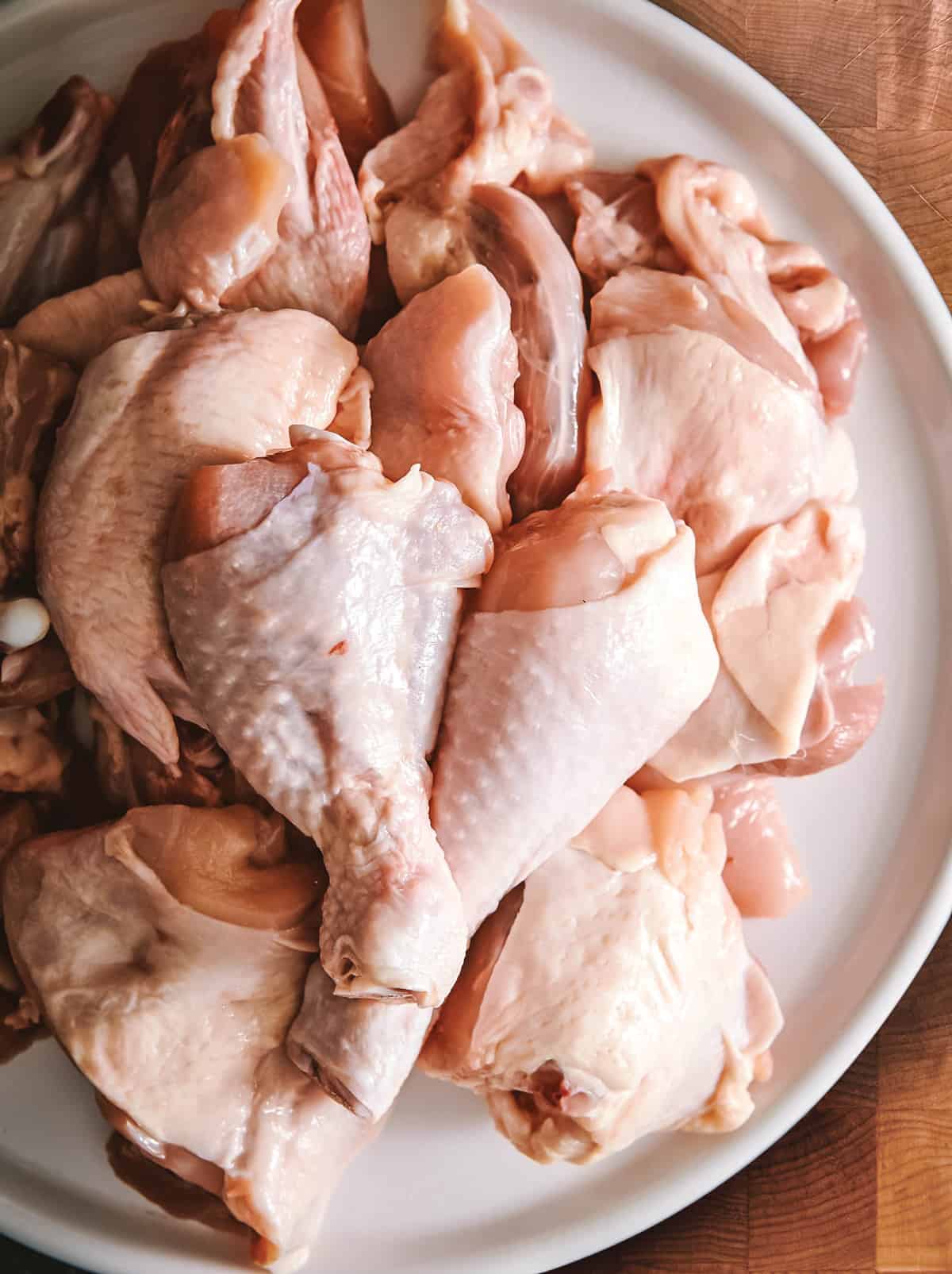 Close up of a plate with a whole chicken cut in chops on a cutting board.