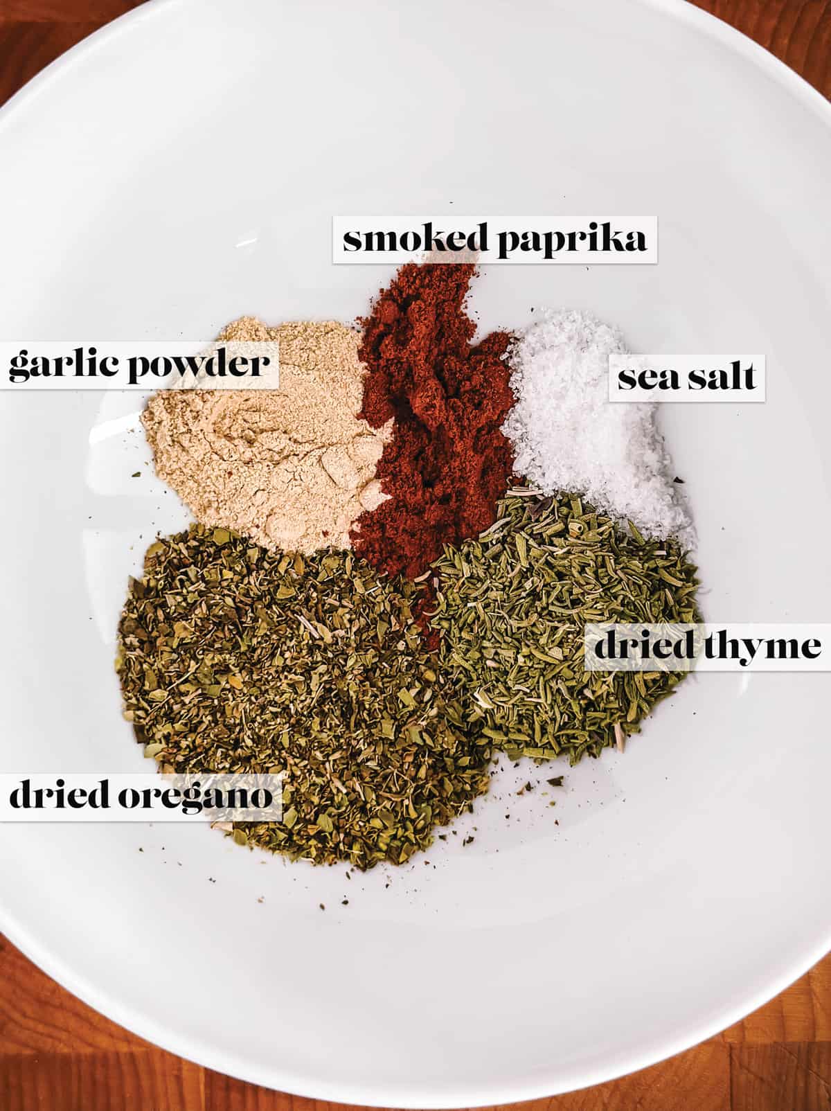 A bowl with dried oregano, thyme, sea salt, garlic powder and smoked paprika.