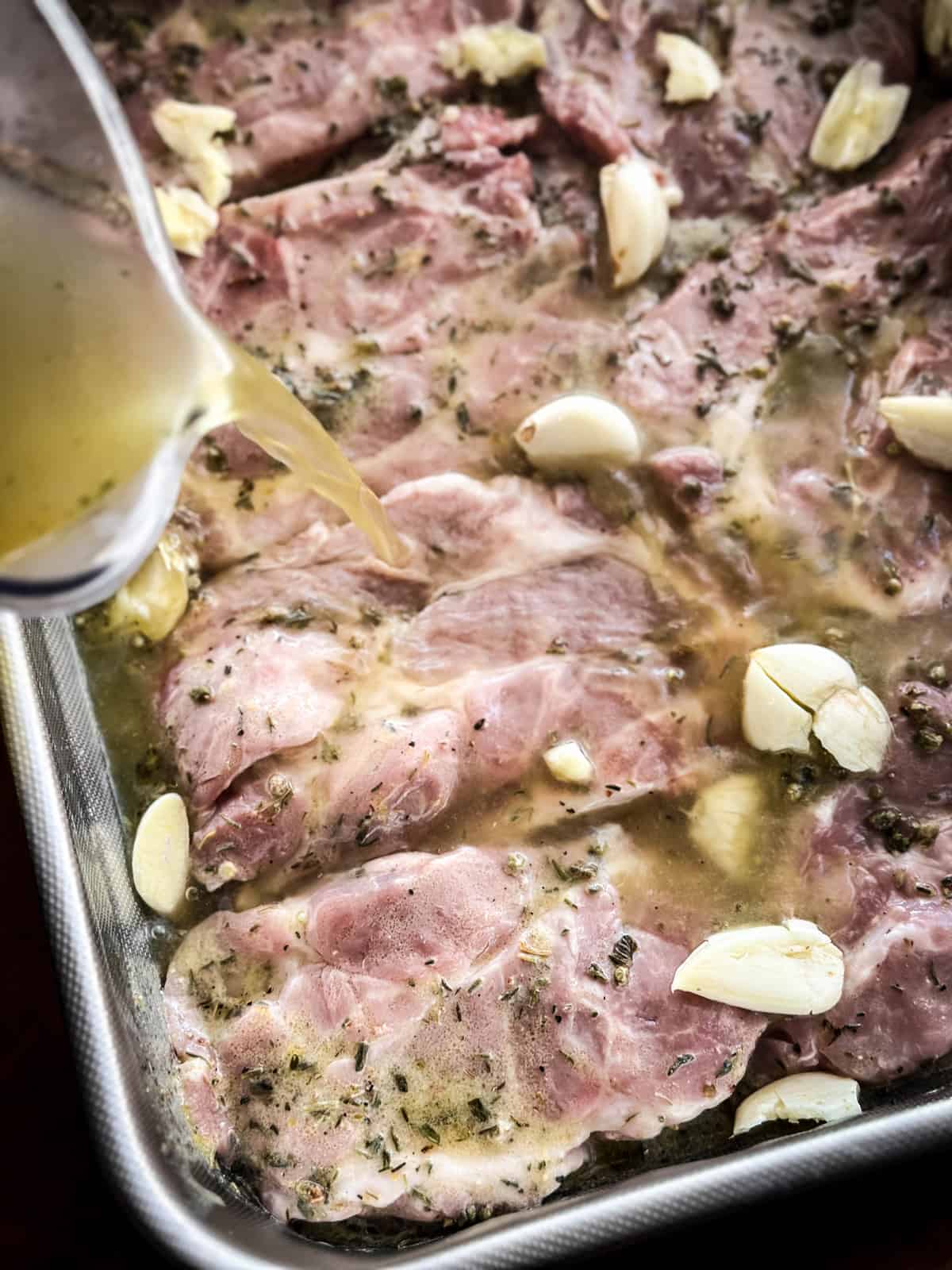 A jug pouring chicken broth on pork steaks.