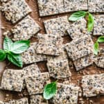 Homemade crackers on parchment paper with fresh basil leaves.