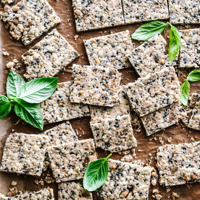 Homemade crackers on parchment paper with fresh basil leaves.