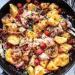 A pan with a roasted chicken, potatoes, cherry tomatoes and pieces of feta cheese and garlic.
