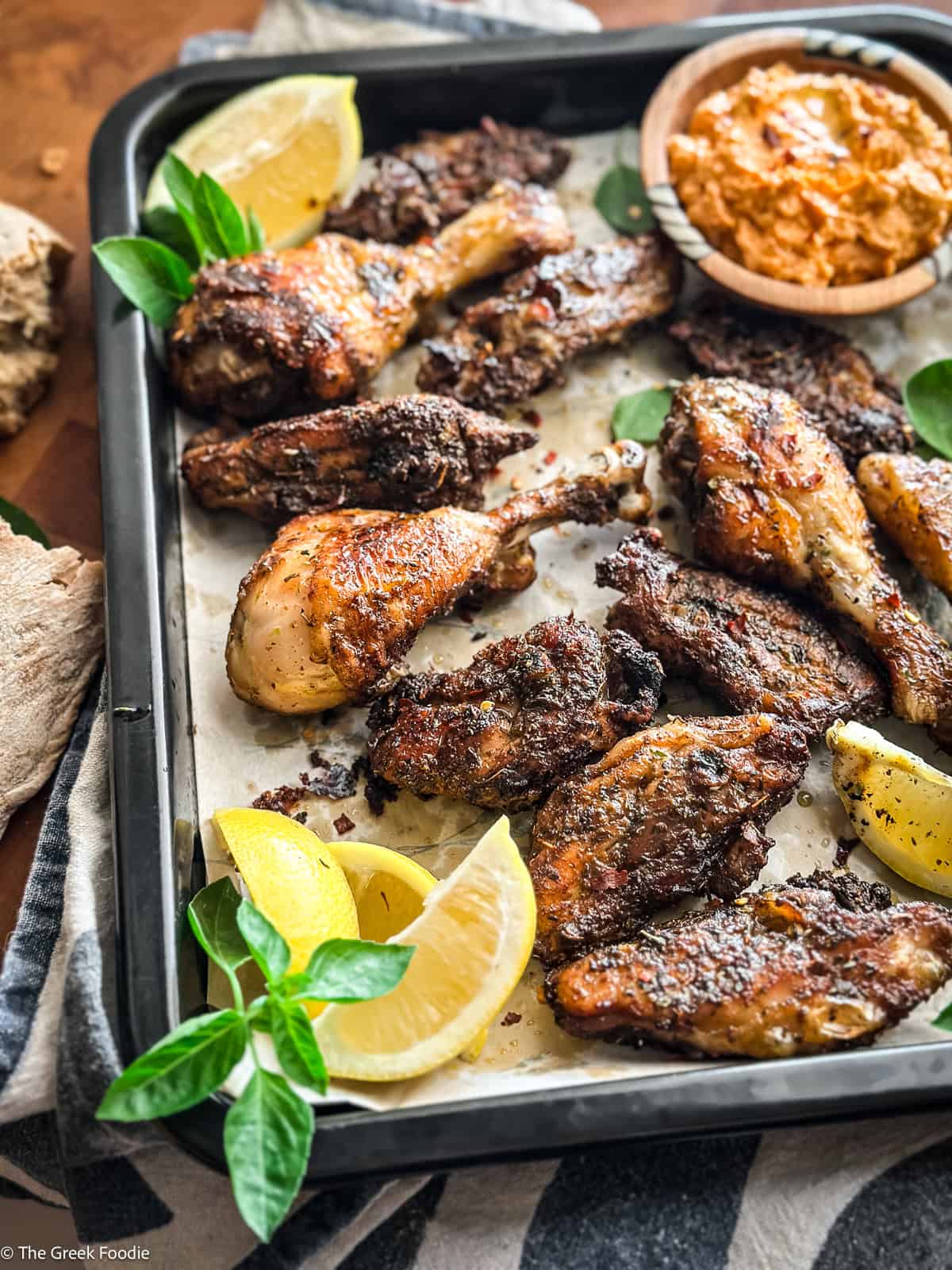 Sheet pan of Greek chicken chops garnished with fresh oregano and lemon
