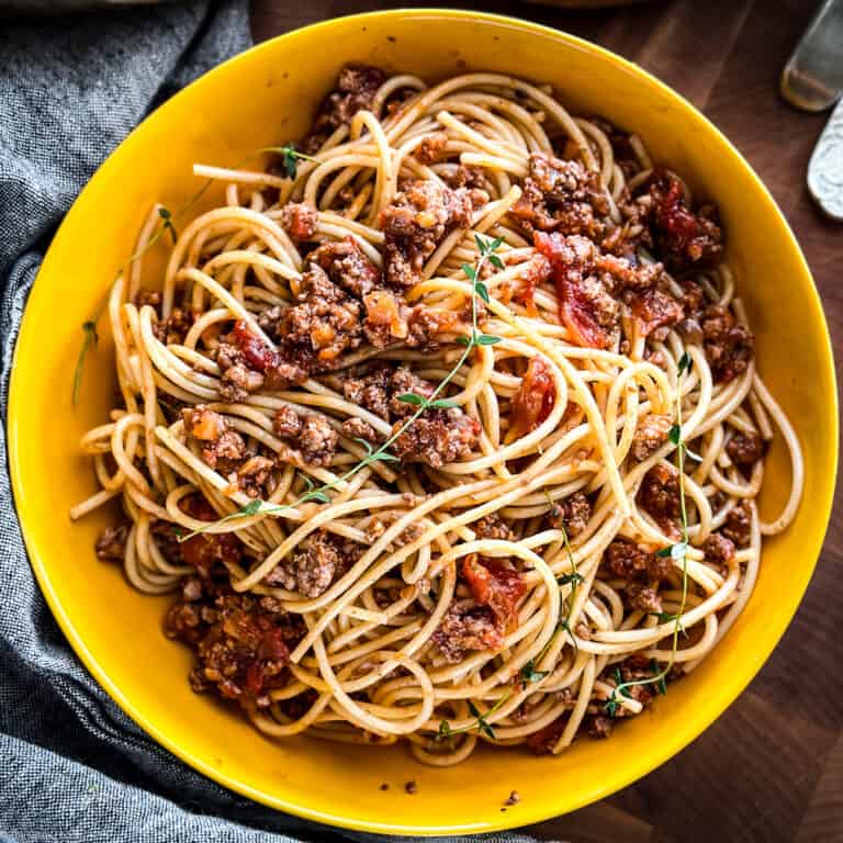 A yellow pasta bowl with Greek spaghetti with meat sauce over a napkin on a table.