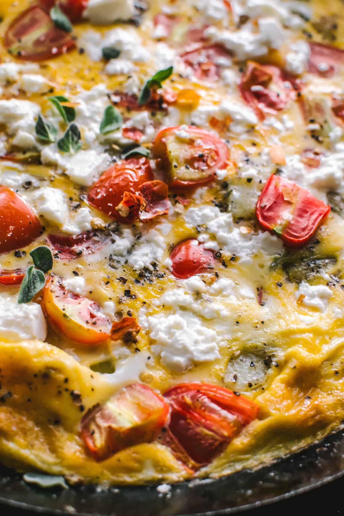 A Greek omelette with feta cheese, cherry tomatoes and fresh herbs in a skillet.