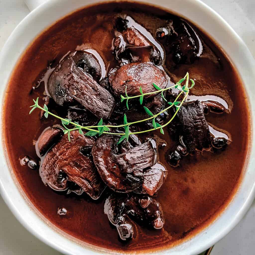 A bowl with marsalla sauce with mushrooms and twigs of thyme on top.