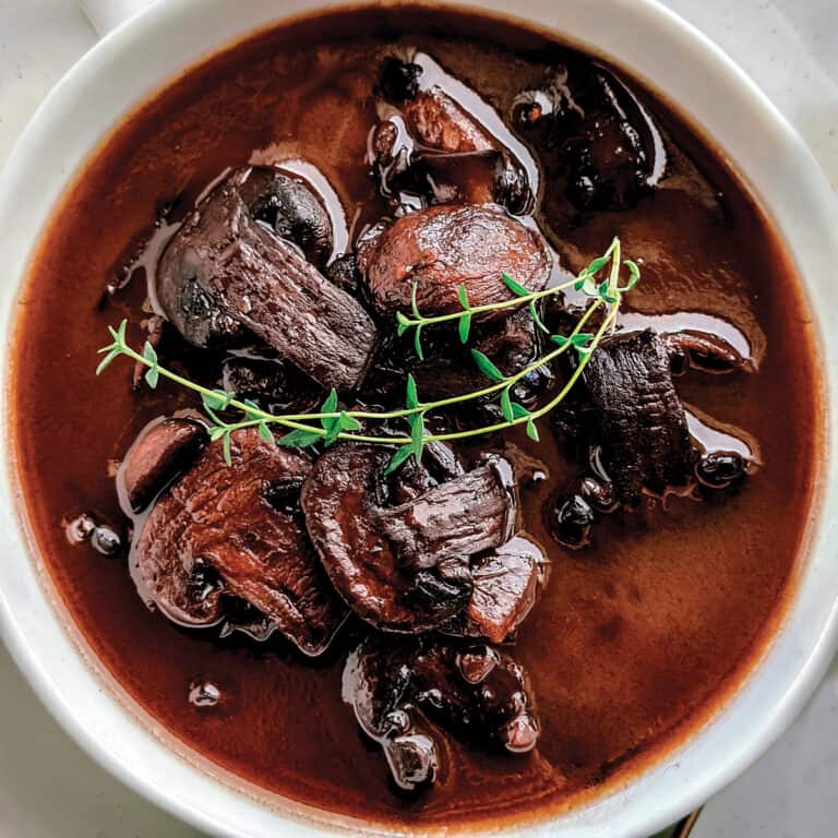 A bowl with marsalla sauce with mushrooms and twigs of thyme on top.