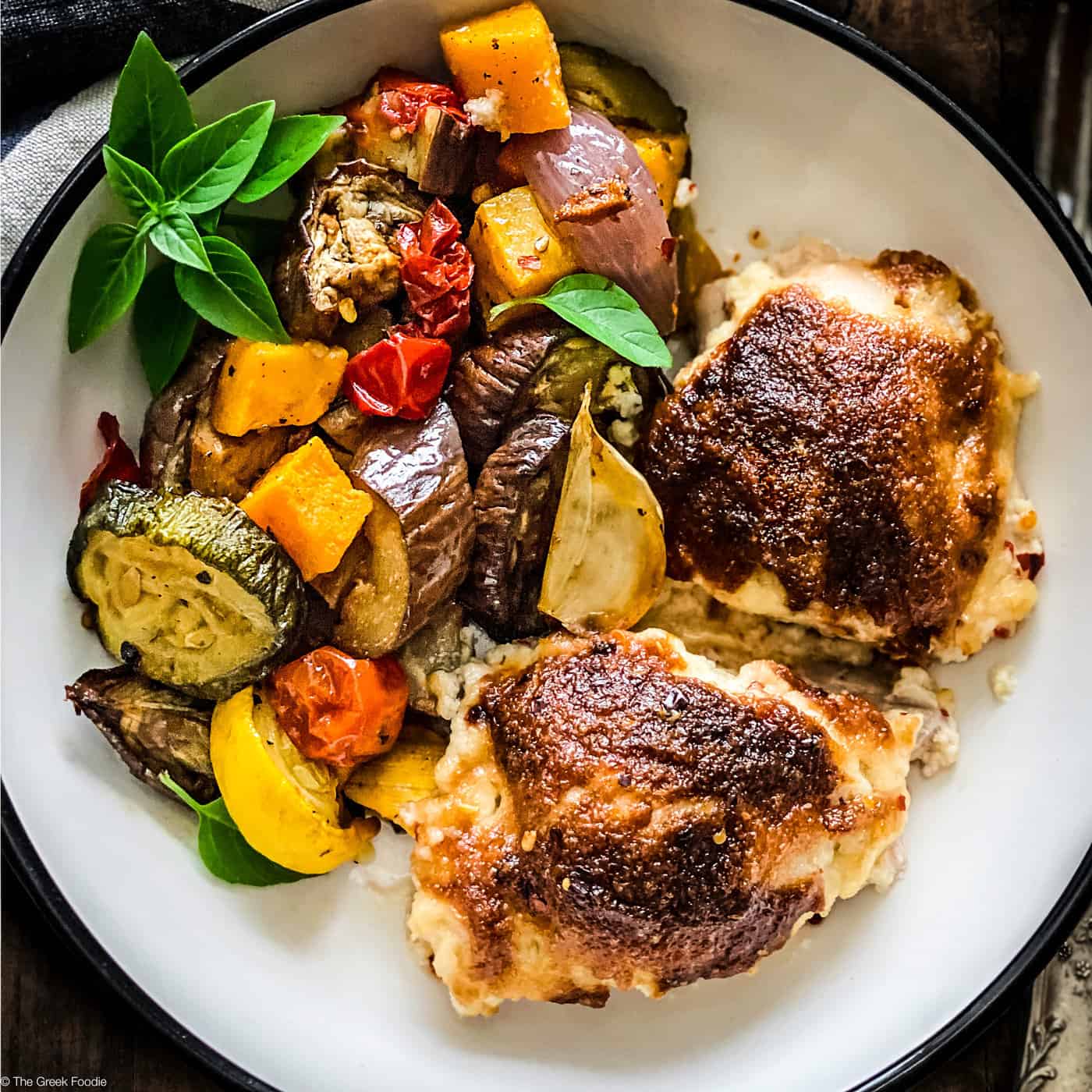 Two pieces of parmesan crusted chicken with mayo and grilled vegetables on a white plate.