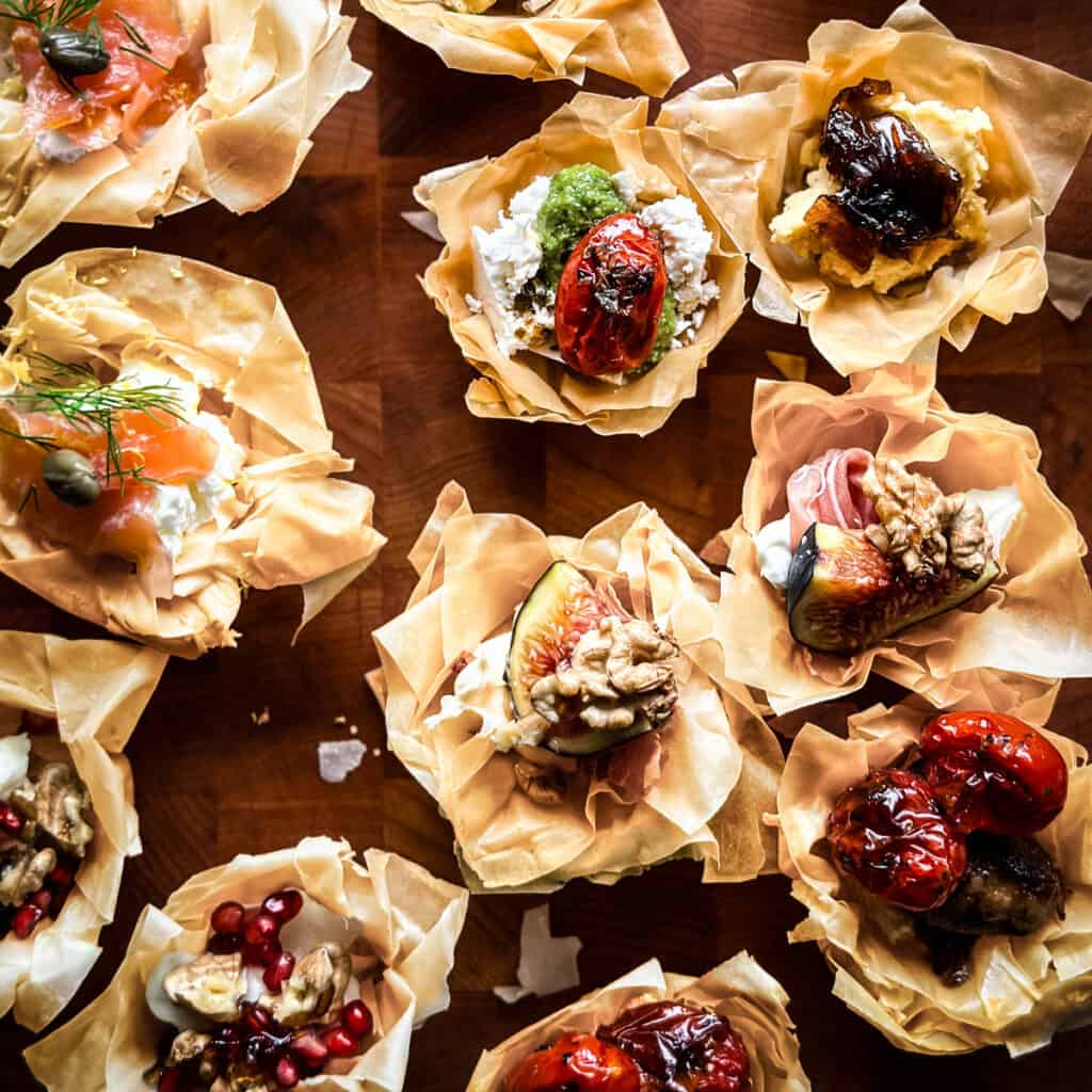 Many phyllo cup appetizers with different fillings on a wooden surface.
