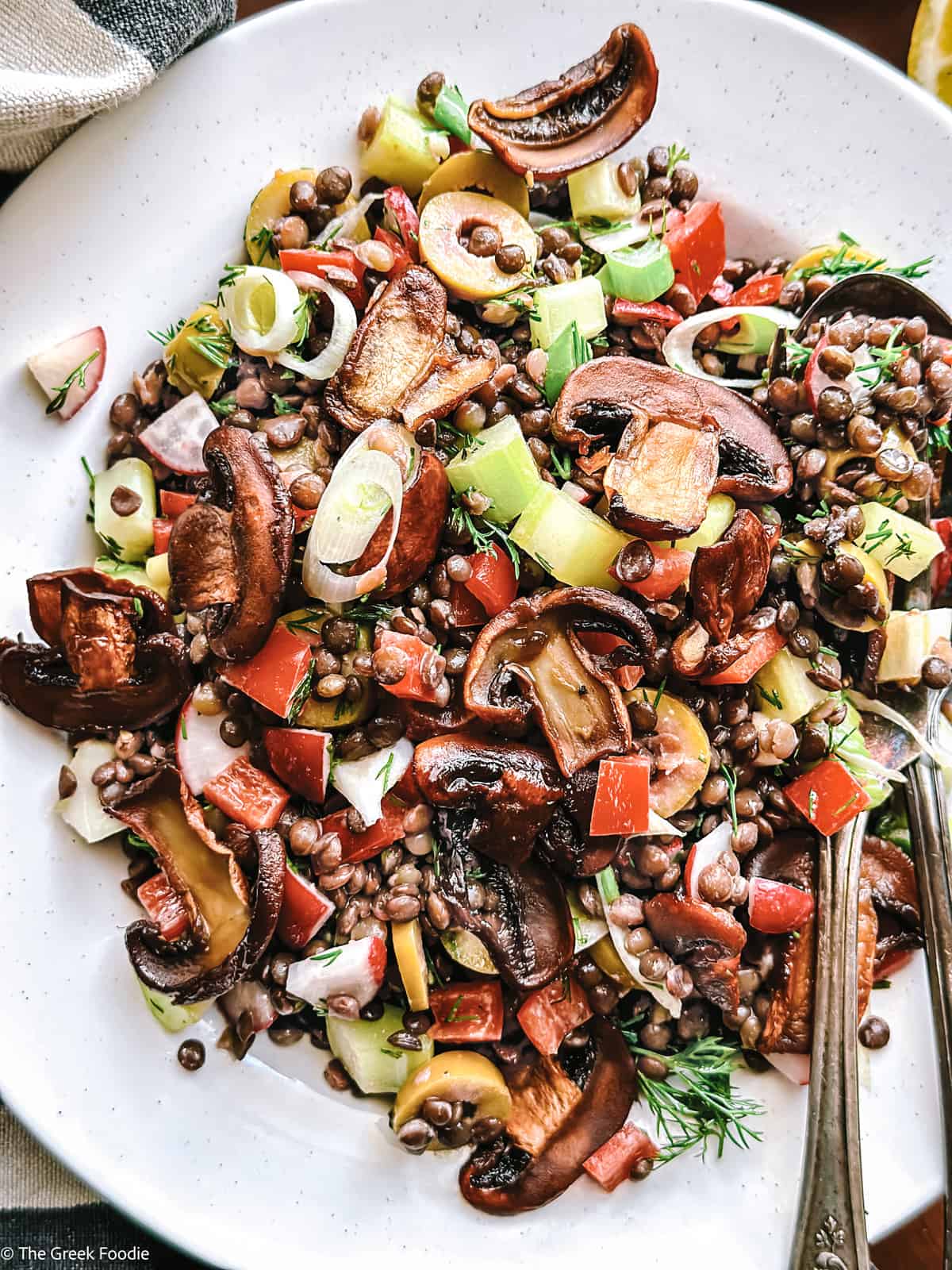 A plate with black lentils, mushrooms, scallions, peppers on a wooden table with a cloth napkin. 