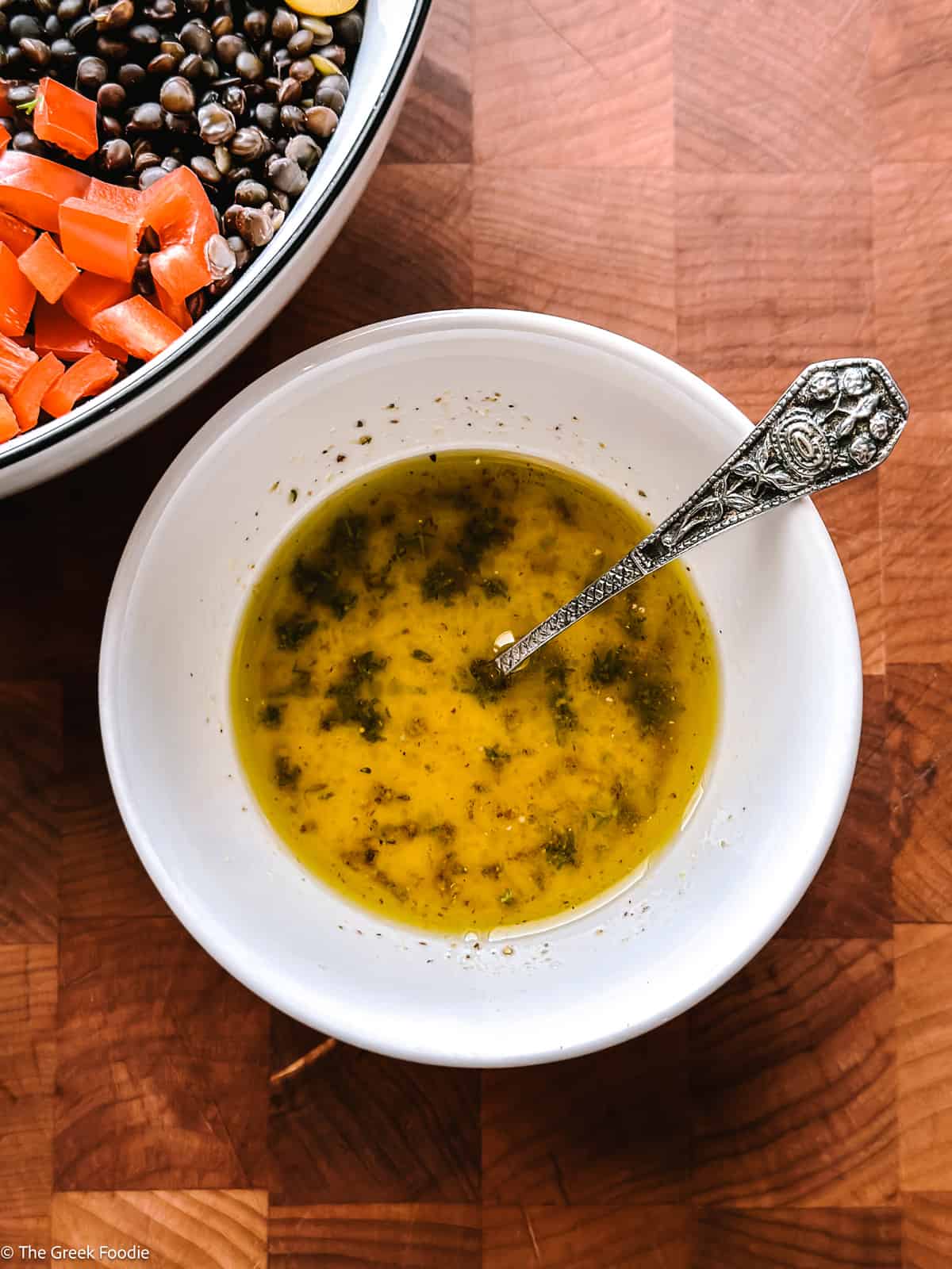 A small bowl with dijon lemon dressing next to a partially viewed salad on a wooden table.