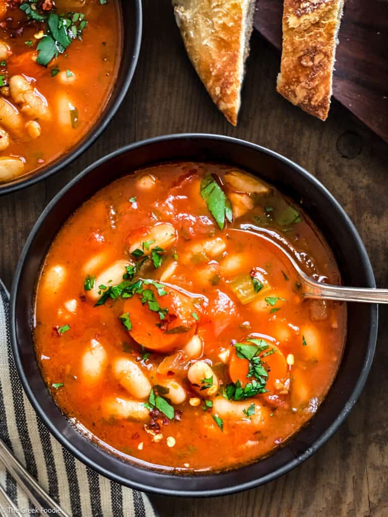 A bowl with fasolada-Greek white bean soup, slices of bread and partial view of another bowl.