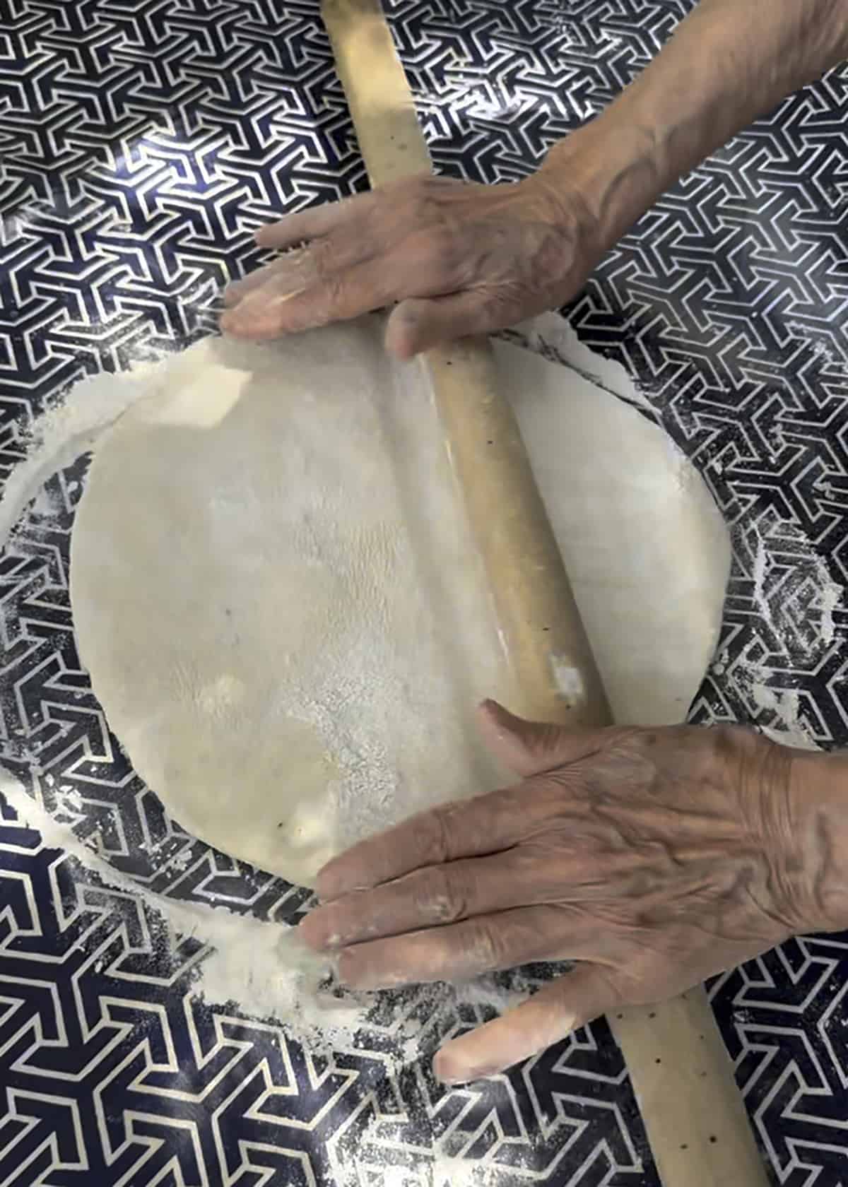 Hands of an elderly woman pressing down a piece of phyllo dough on a table.
