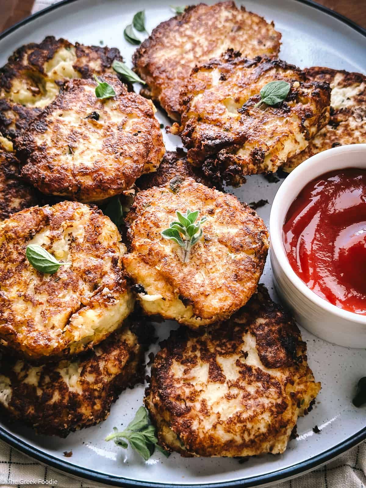 Cauliflower fritters on a plate with a cup with ketchup.