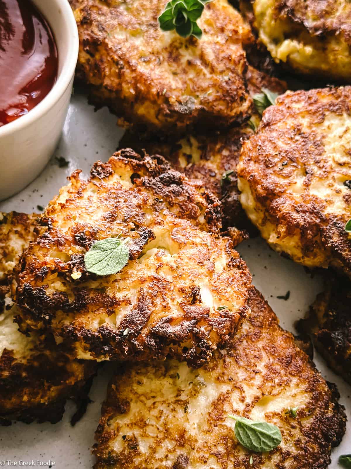 Cauliflower fritters on a plate with a cup with ketchup.