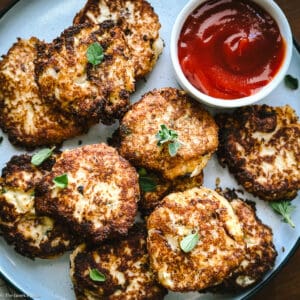 Cauliflower fritters on a plate with a cup with ketchup.