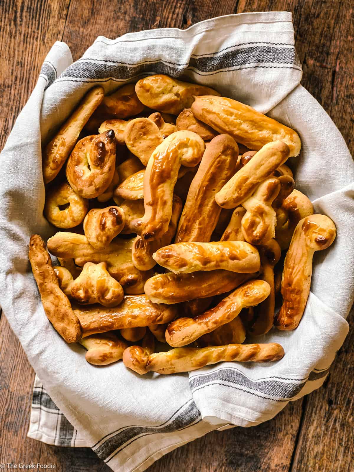 Greek Easter Cookies-Koulourakia wrapped in a cloth, in a bowl on a wooden table. Overhead view.