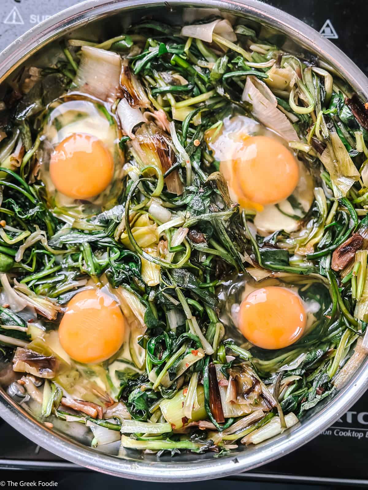 Four eggs and greens in a skillet