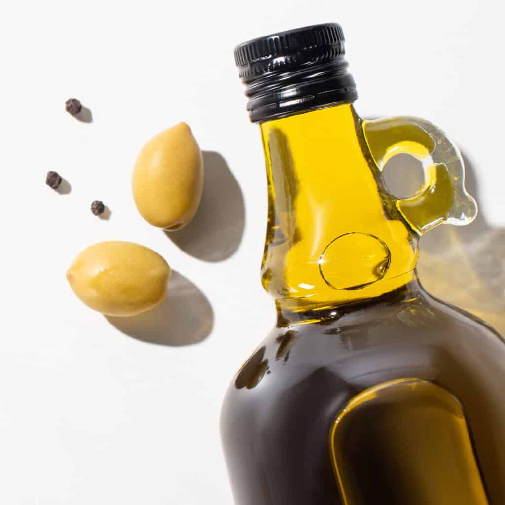 A glass bottle of olive oil and two olives.
