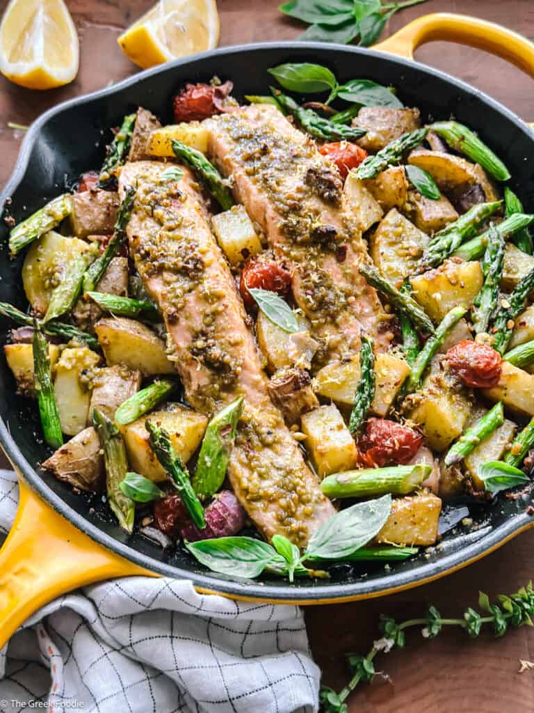 Greek salmon recipe with pesto, cherry tomatoes, and asparagus in a skillet