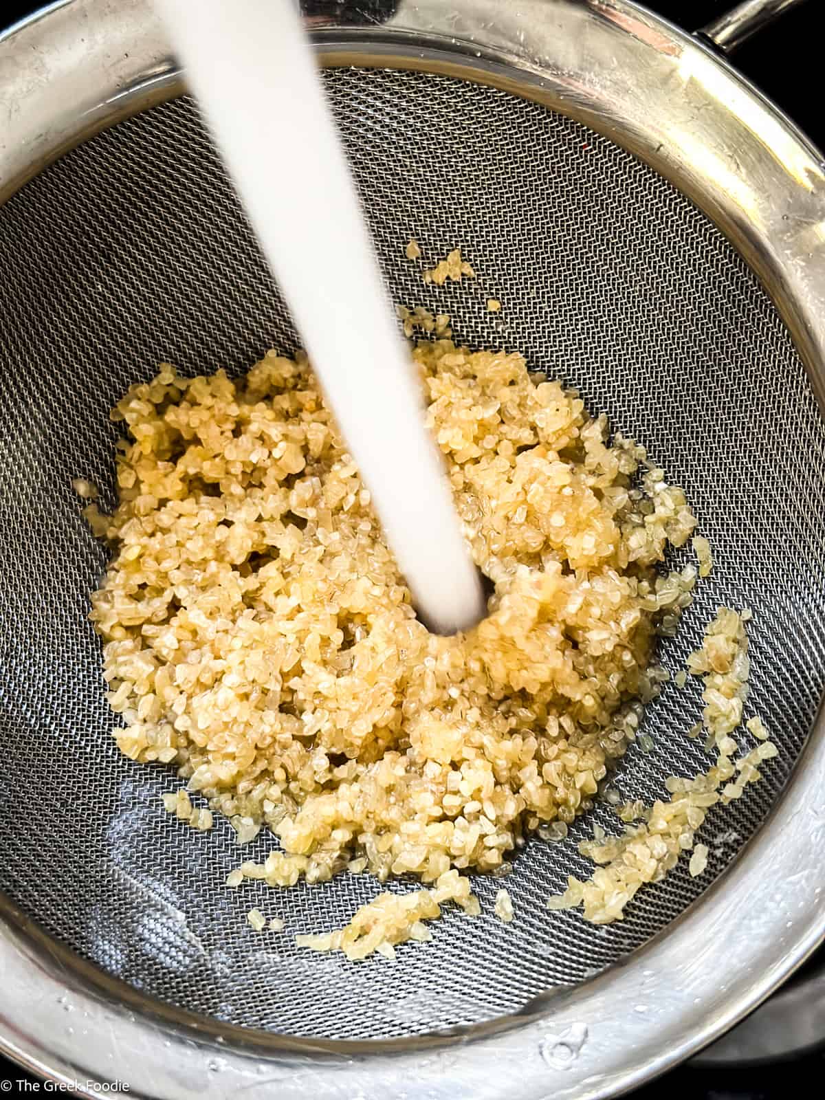 Bulgur wheat in a sieve and water running on it.