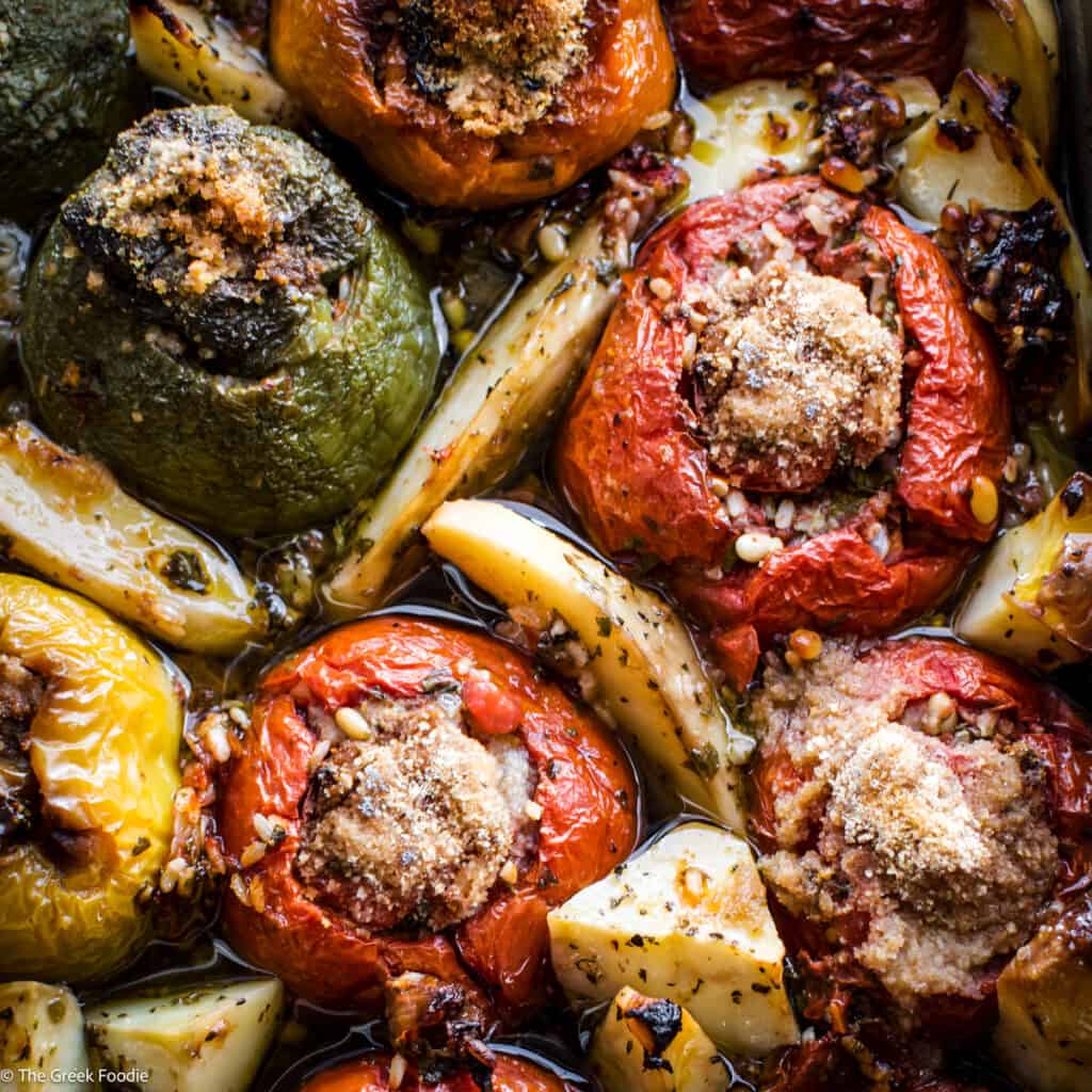 A baking pan with gemista-stuffed tomatoes and bell peppers, potatoes and fresh herbs.