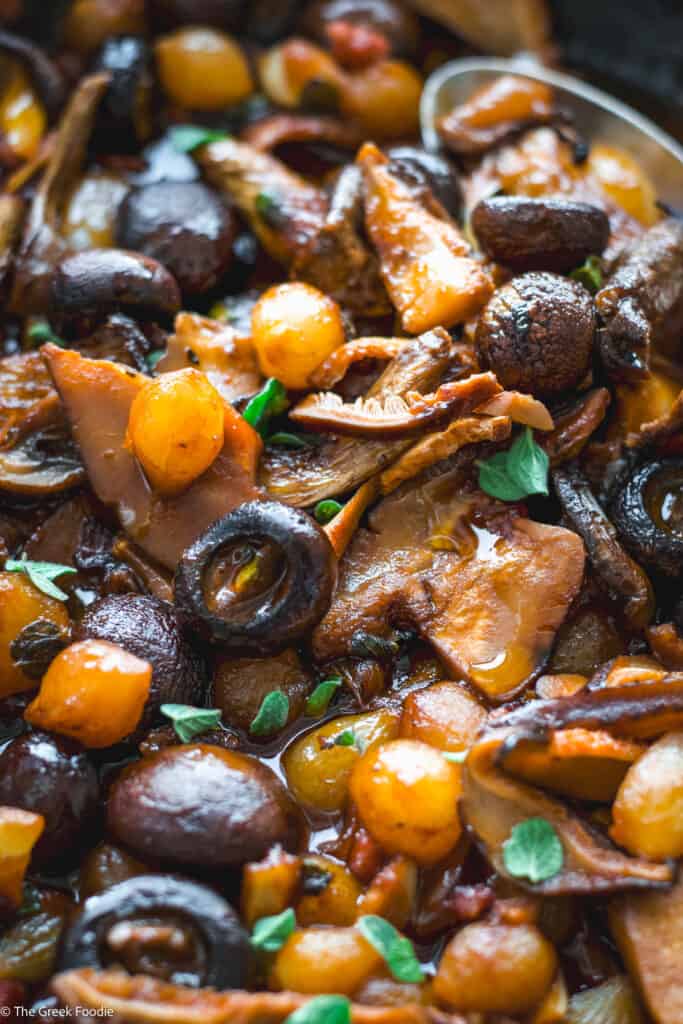 Close up of a mushroom stew with herbs and a spoon.
