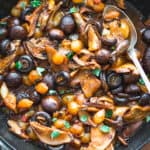 A skillet with mushroom stew stifado a spoon, over a cloth napkin.